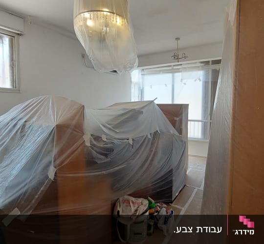 חדר עם רהיטים מכוסים בניילון ודליי צבע על הרצפה